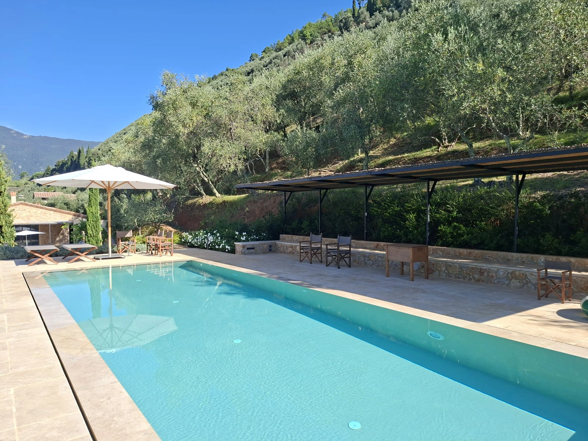 Piscina a sfioro con solarium in pietra naturale e vista sulla collina di ulivi